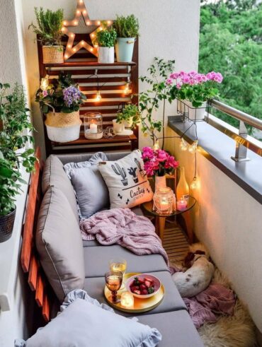 Pequena varanda de apartamento com sofá, almofadas, vasos com plantas e flores
