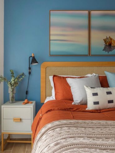 Quarto de casal com parede azul atrás da cama, cabeceira com palhinha e mesa de cabeceira branca