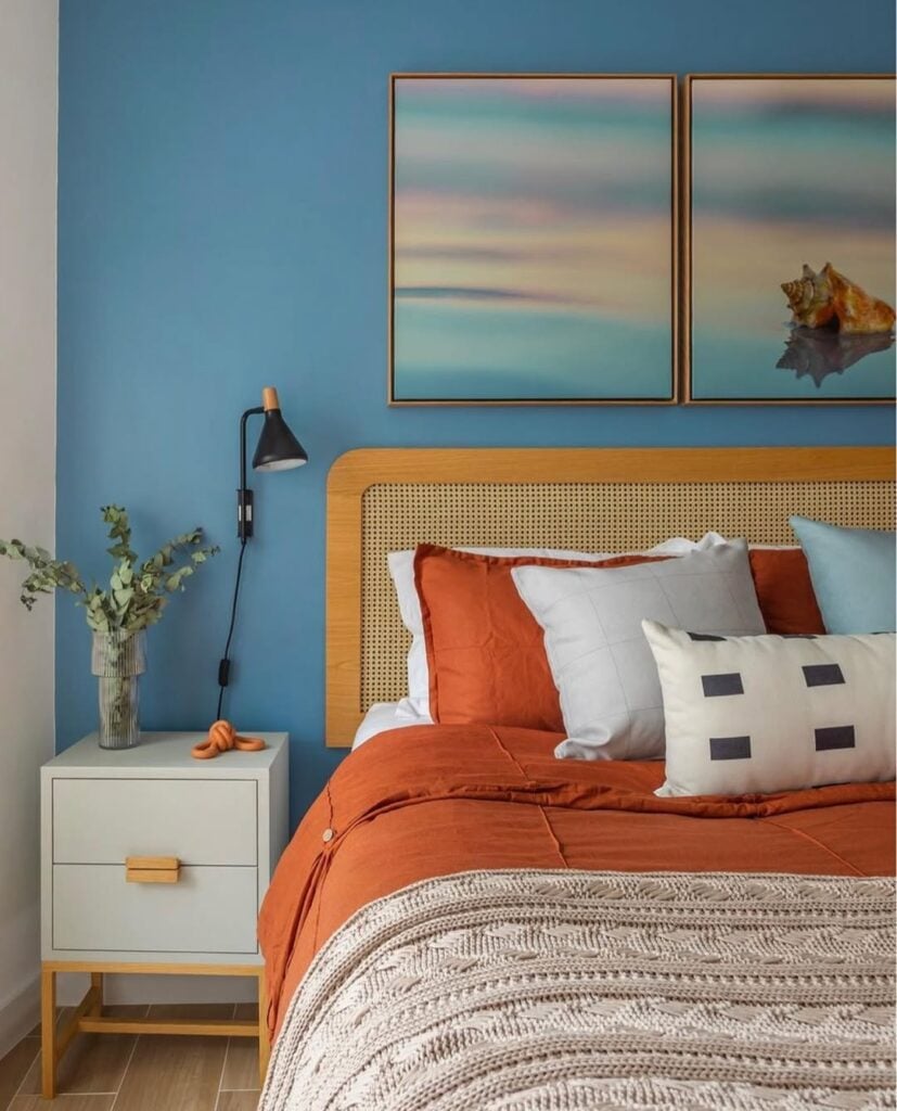 Quarto de casal com parede azul atrás da cama, cabeceira com palhinha e mesa de cabeceira branca