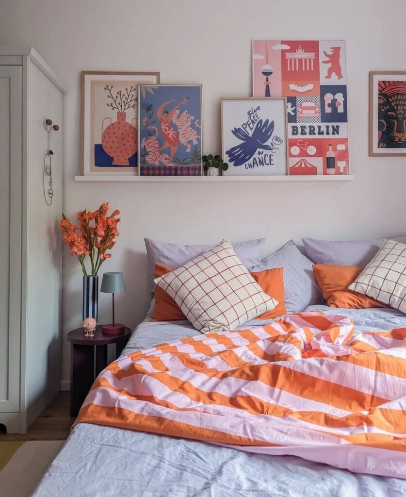 Quarto de casal com prateleira e quadros, mesa de cabeceira com flores laranja
