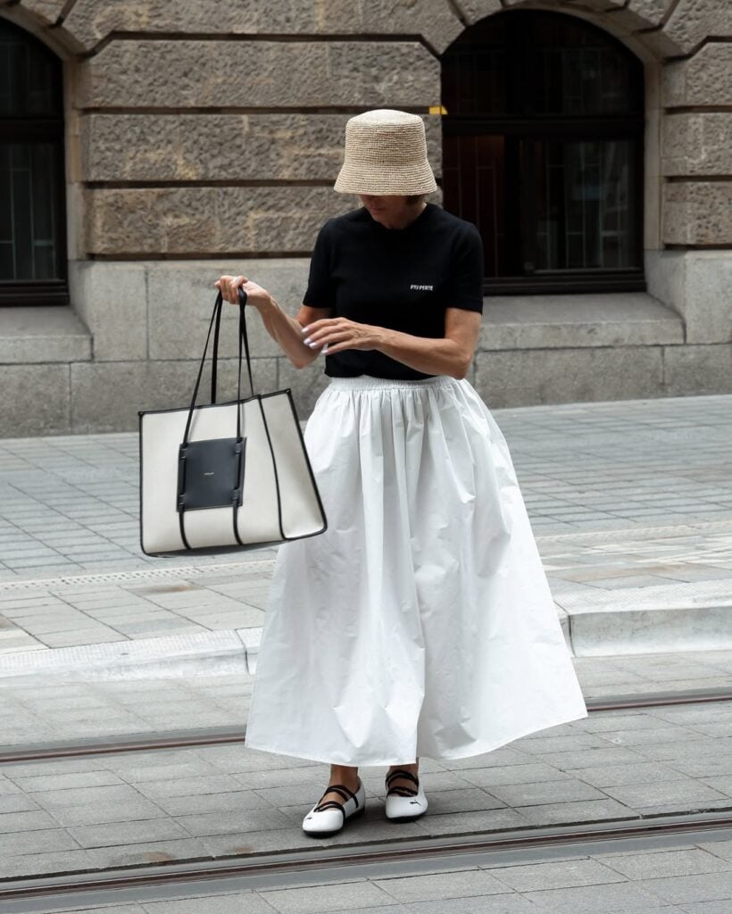 Mulher jovem, magra e de pele clara. Ela veste camiseta preta e maxi skirt