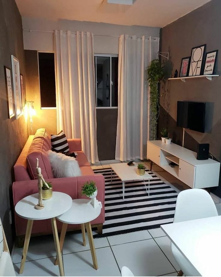Sala pequena com cortina branca, tapete listrado e sofá rosa