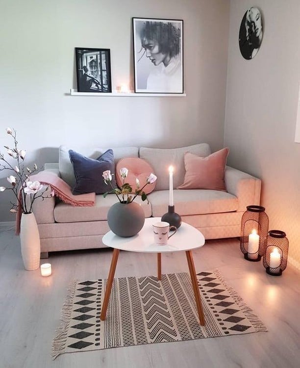 Sala com sofá claro, almofadas rosa, mesa de centro branco e objetos decorativos