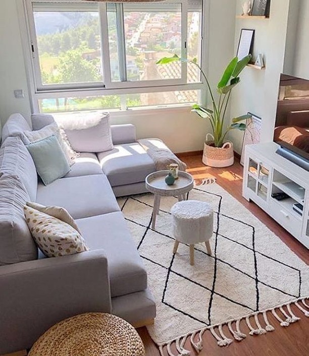 Sala com ampla janela, sofá claro, tapete bege e preto e mesa de centro pequena
