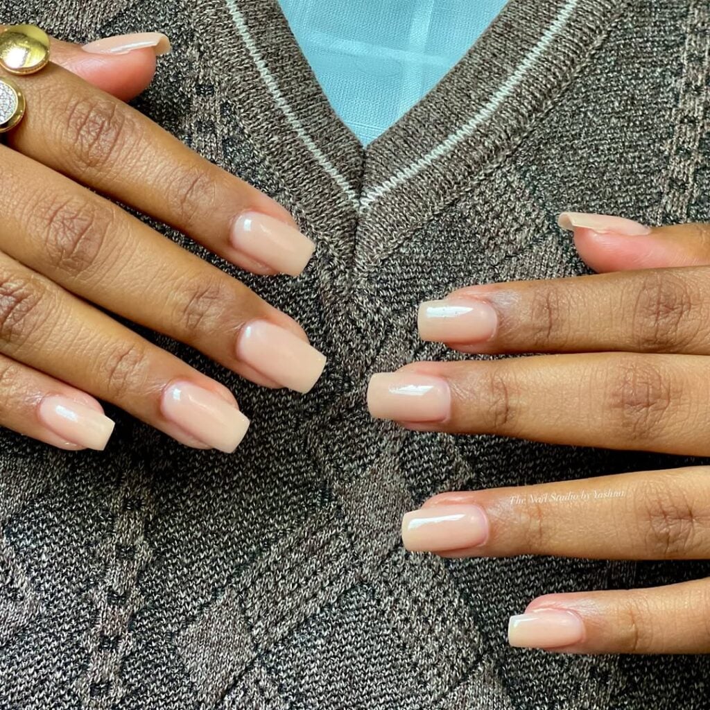 Mãos de pele preta, com anel em dourado e unha quadrada nude-claro 