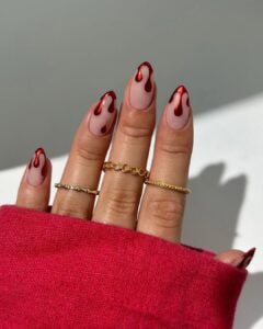 Mãos de pele clara, com anéis em dourado e unha nude com esmalte vermelho efeito sangue escorrendo