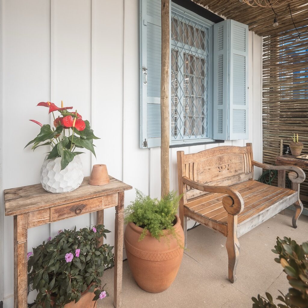 Varanda gourmet charmosa com parede de madeira, móveis de madeira e vaso de cerâmica com plantas e flores