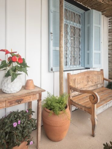 Varanda gourmet charmosa com parede de madeira, móveis de madeira e vaso de cerâmica com plantas e flores