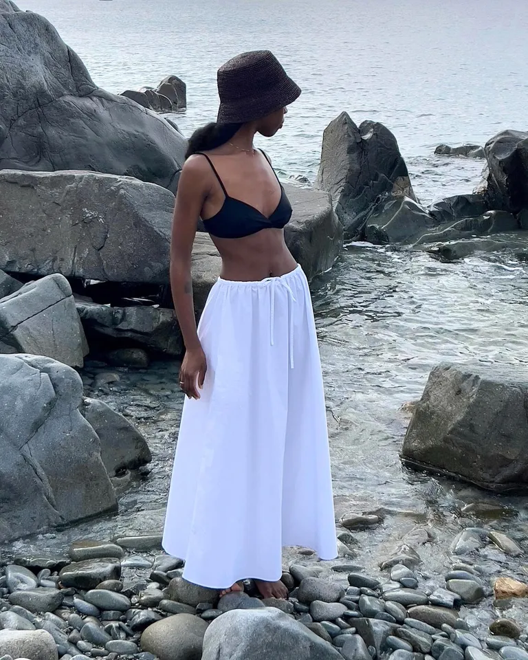 Mulher jovem com saia longa branca e biquíni preto