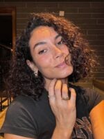 Mulher com blusa cinza e cabelo cacheado escuro e curto