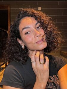 Mulher com blusa cinza e cabelo cacheado escuro e curto