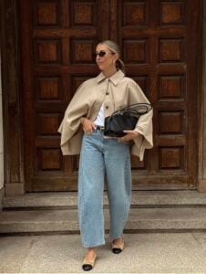 Mulher de pele clara, com blusa branca, casa bege e calça barrel jeans com sapatilha