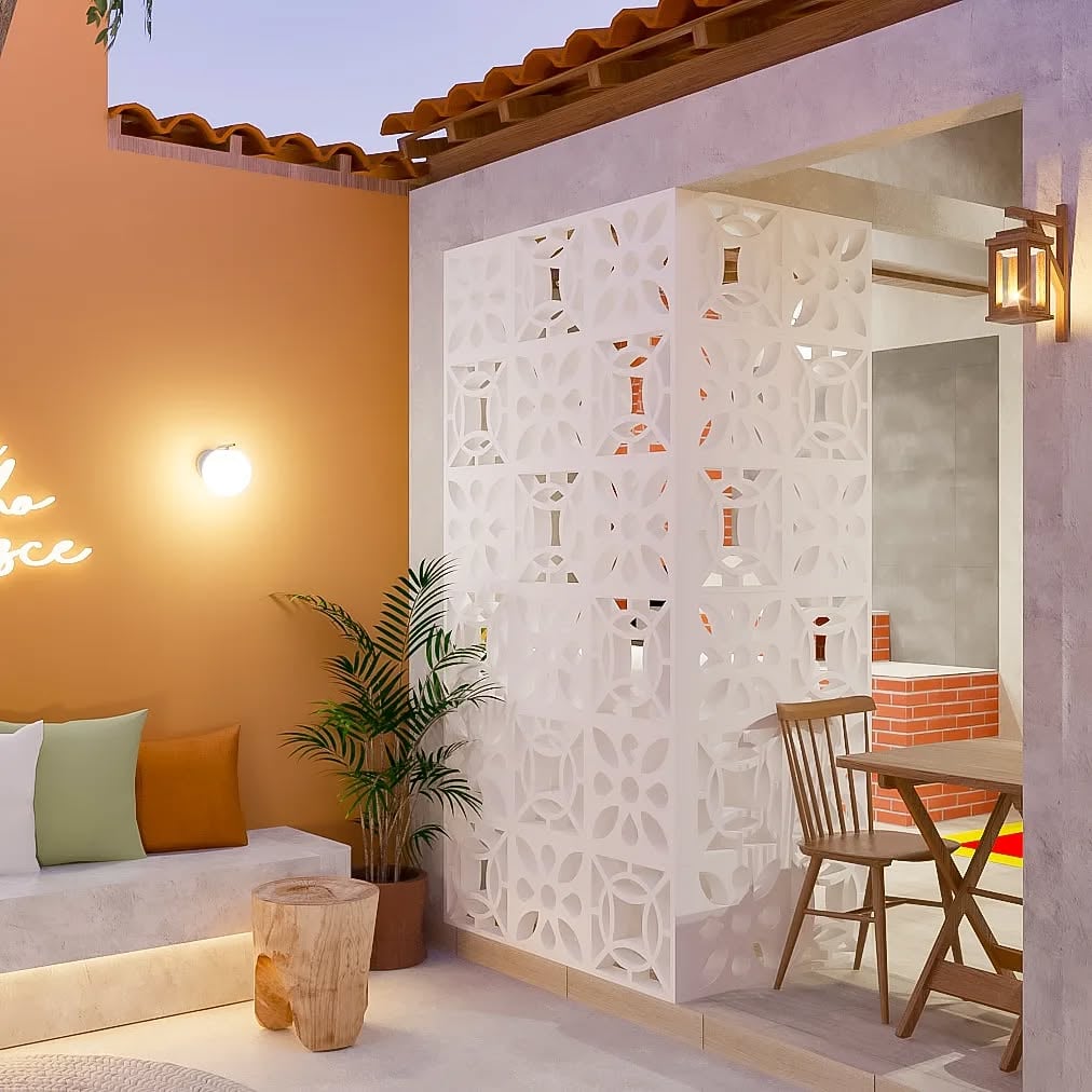 Ambiente externo com sofá, almofadas, parede terracota e cobogó branco