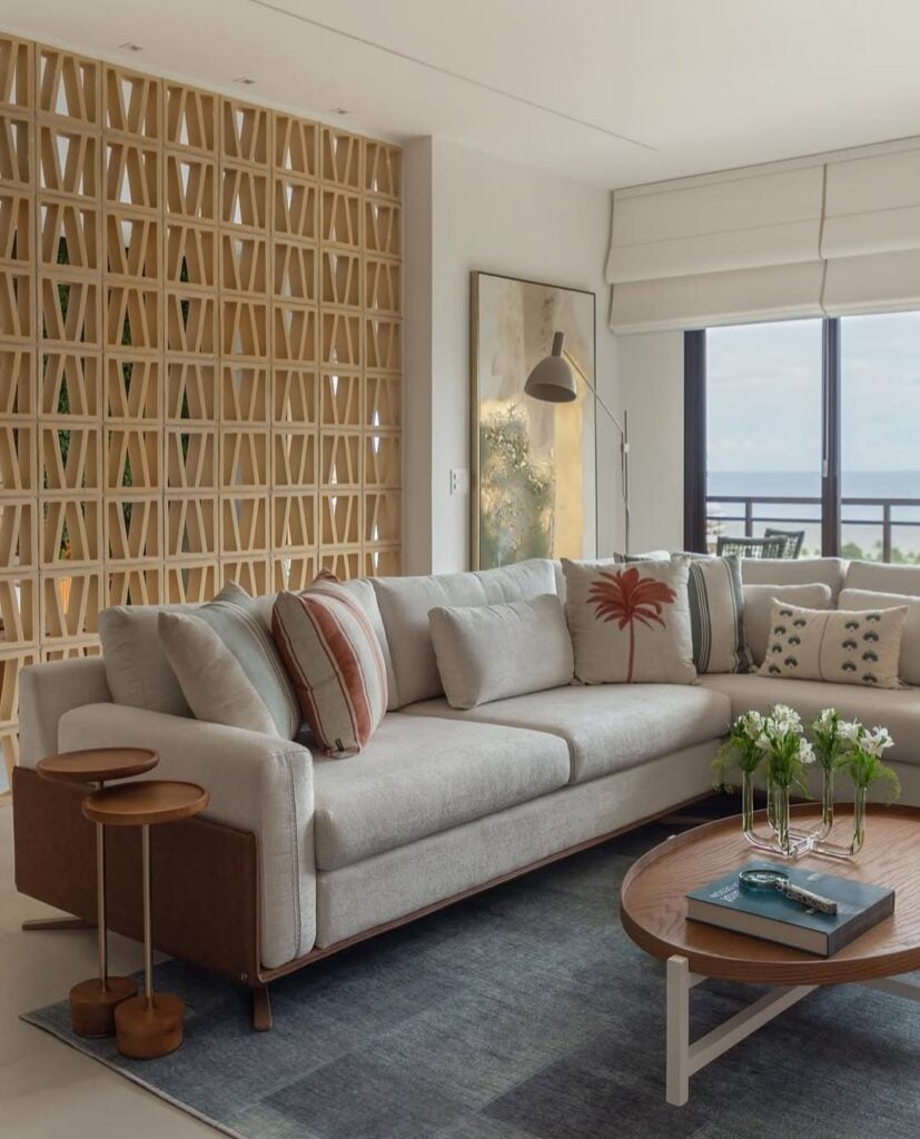 Sala de estar com sofá em L, mesa de centro e mesinhas laterais e cobogó em cor clara