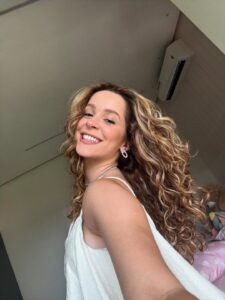Mulher de pele clara, com blusa branca e cabelo ondulado com luzes