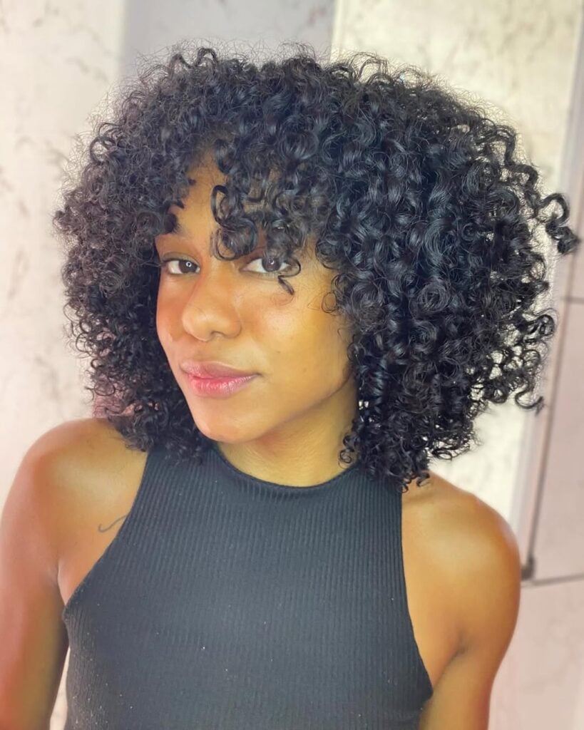 Mulher de pele preta, com blusa preta e cabelo cacheado com corte arredondado 