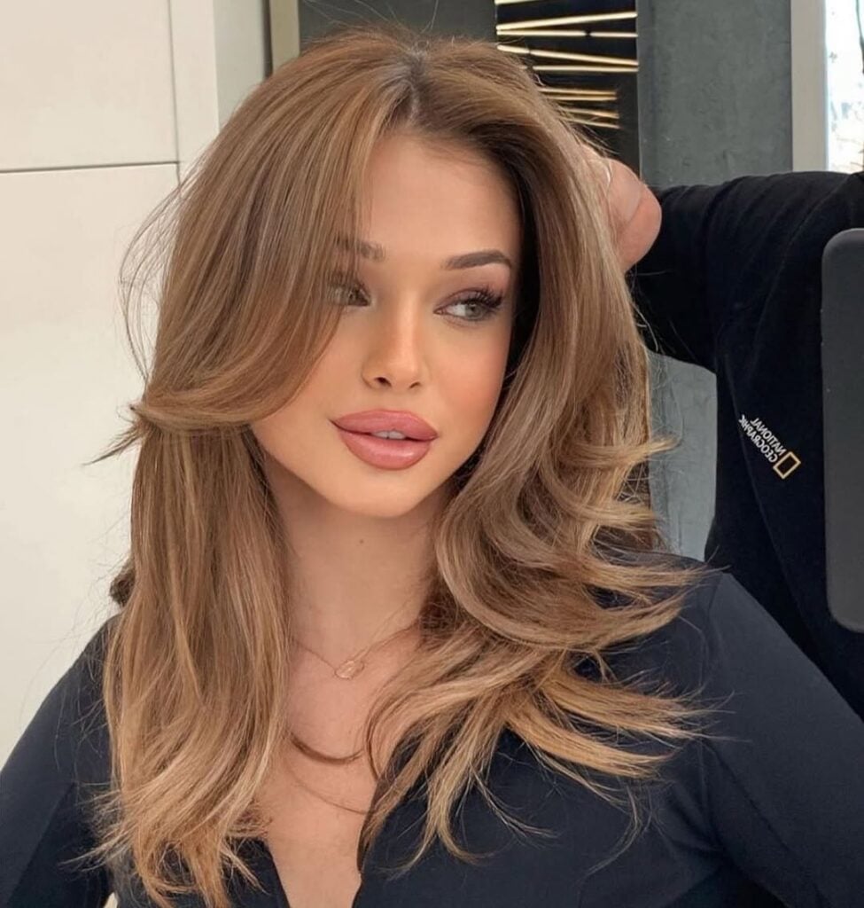 Mulher de pele clara, com roupa preta e cabelo claro médio com corte em camadas