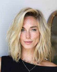 Mulher de pele clara, com blusa preta, acessórios e cabelo loiro em corte long bob
