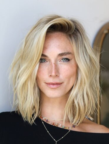 Mulher de pele clara, com blusa preta, acessórios e cabelo loiro em corte long bob