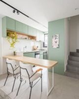 Cozinha verde-água com mesa de madeira ligada à parede e cadeiras de metal preto com estofados claros