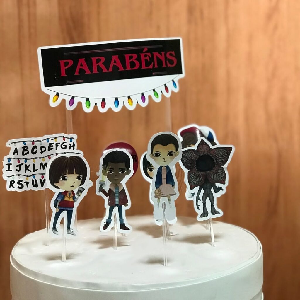 Bolo branco com bonequinhos de papel de personagens de Stranger Things