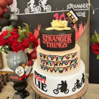 Decoração de aniversário tema de Stranger Things, com bolo de três andares e biscoitos temáticos