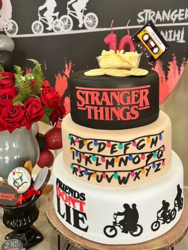 Decoração de aniversário tema de Stranger Things, com bolo de três andares e biscoitos temáticos