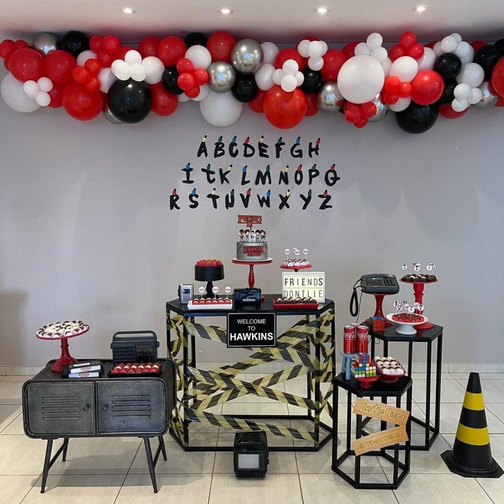 Decoração de aniversário Stranger Things com balões pretos, vermelhos e brancos, rádio, telefone e tv antigos