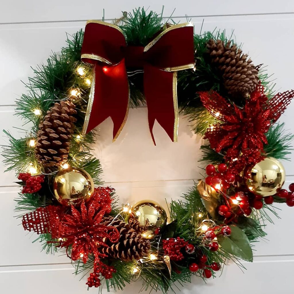 Guirlanda de Natal decorada com flores vermelhas, esferas douradas, pinhas e luzinhas