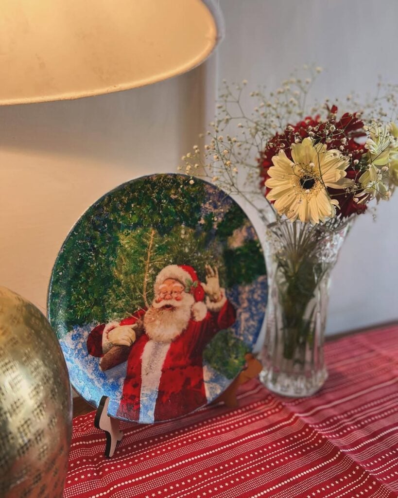 Prato decorado com Papai Noel ao lado de um vaso de vidro transparente com flores