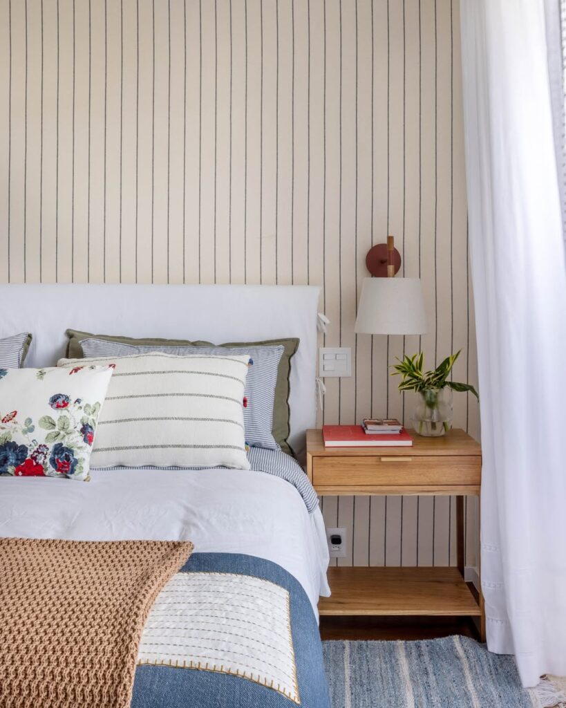 Quarto com mesa de cabeceira de madeira, arandela e manta de tricô na cama
