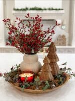 Bandeja decorada com vela, vaso com florzinhas vermelhas e árvores natalinas de fibras naturais
