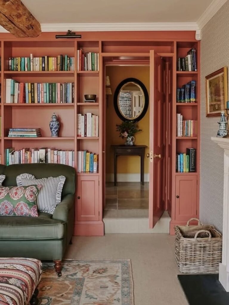 Sala de estar com estante de livros rosa, sofá e almofadas verde