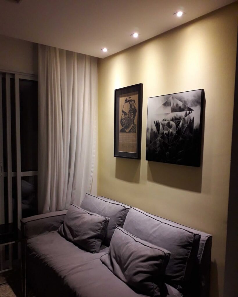 Sala pequena com sofá e quadros acima destacados por iluminação