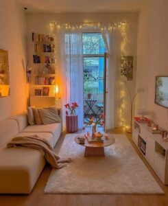 Sala pequena charmosa com móveis brancos, tapete, mesa de centro, estante com livros e sacada