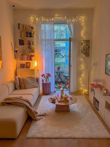 Sala pequena charmosa com móveis brancos, tapete, mesa de centro, estante com livros e sacada