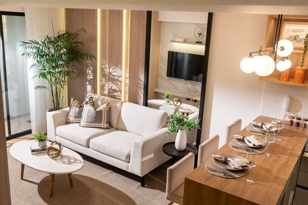 Sala com sofá bege com espelho atrás, mesa lateral preta e mesa de centro branca