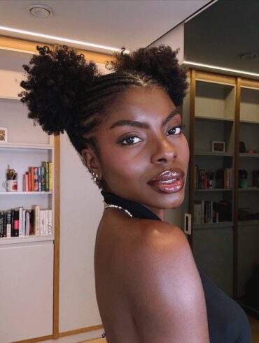 Mulher de pele preta, com blusa preta e cabelo crespo com penteado space buns