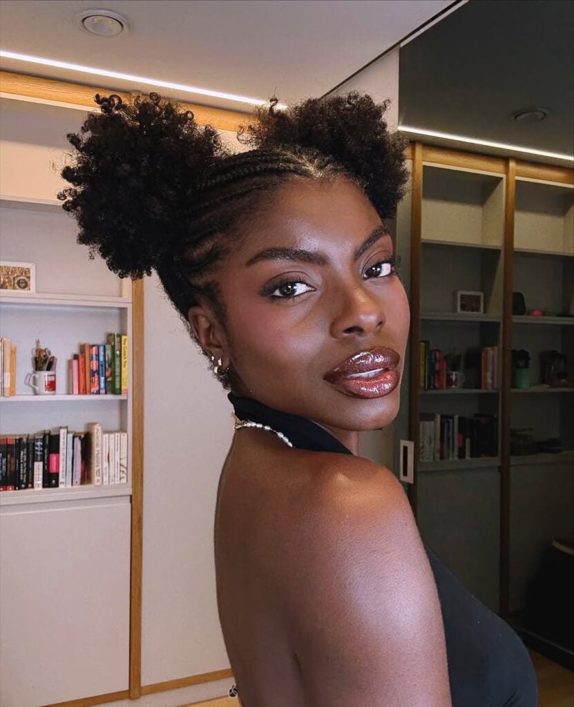 Mulher de pele preta, com blusa preta e cabelo crespo com penteado space buns