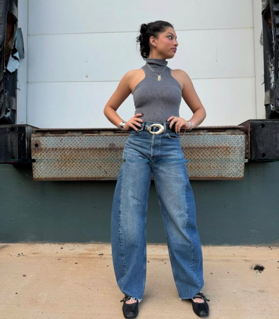 Mulher de pele preta, com blusa cinza e calça jeans barrel com sapatilha