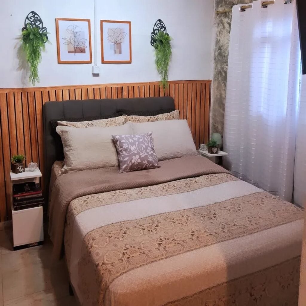 Quarto com meia parede ripada atrás da cama, quadros e plantas pendentes na decoração