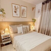 Quarto em tons claros com meia parede ripada, mesas de cabeceiras brancas com pés palitos e plantas pendentes