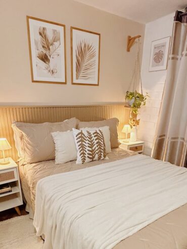 Quarto em tons claros com meia parede ripada, mesas de cabeceiras brancas com pés palitos e plantas pendentes