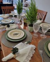 Mesa de madeira com sousplats cinza, pratos verde e pratos menores com pinheirinhos