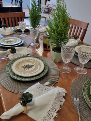 Mesa de madeira com sousplats cinza, pratos verde e pratos menores com pinheirinhos