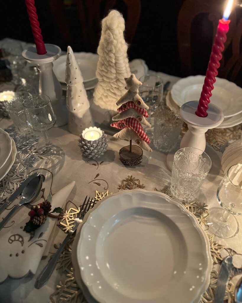 Mesa posta de Natal com toalha branca, castiçal com vela vermelha e árvores natalinas como enfeites
