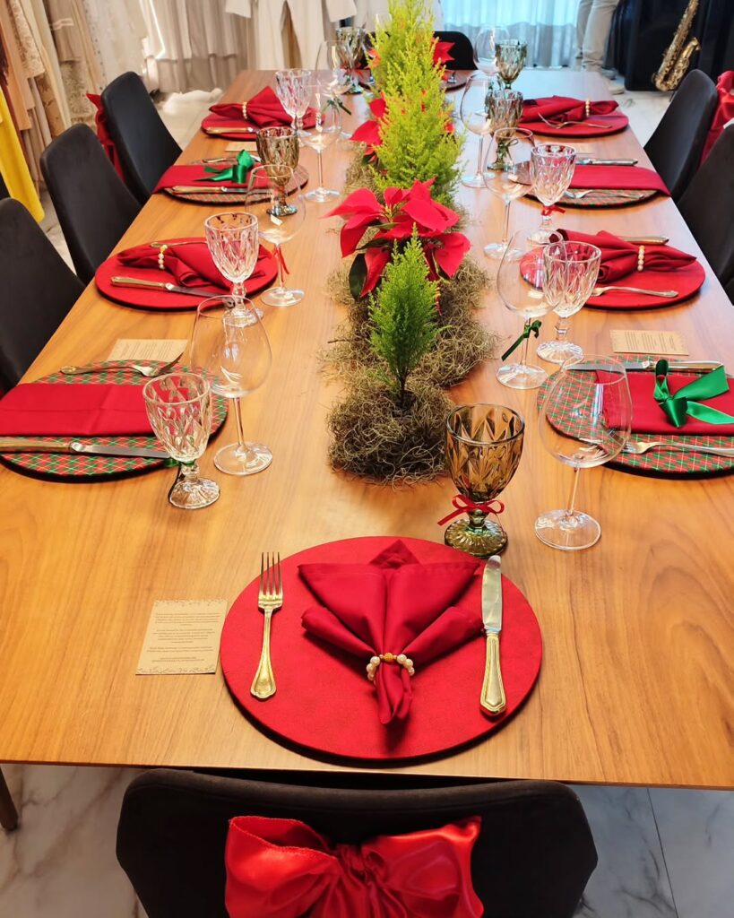 Mesa de madeira decorada para o Natal, com ramos verdes, sousplats e guardanapos vermelhos