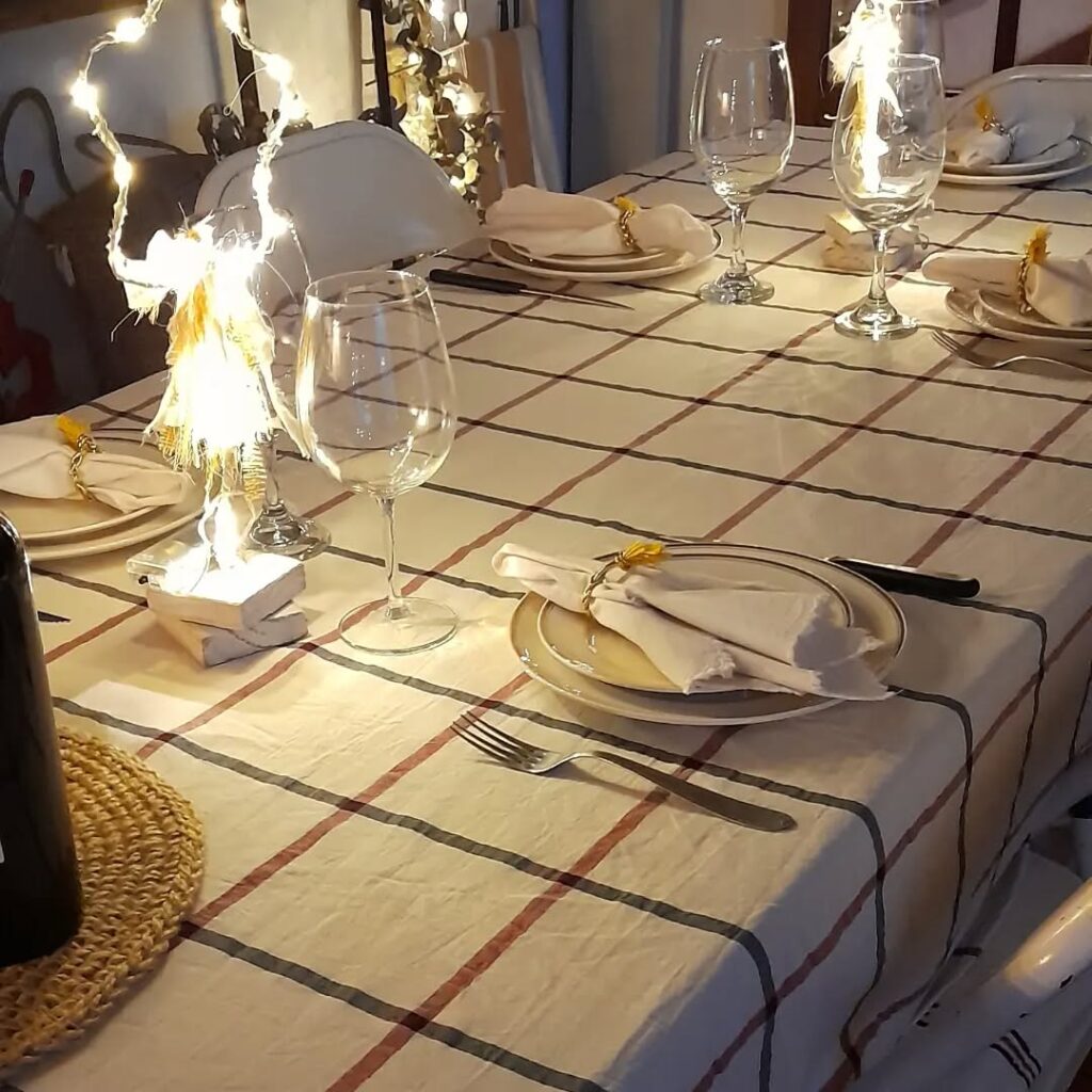 Mesa simples de Natal com toalha branca xadrez, pratos brancos com guardanapos e anel com flor amarela