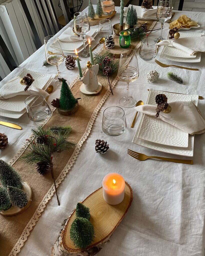 Mesa posta de Natal com toalha e pratos brancos, pequenos pinheiros e velas