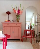 Balcão de madeira rosa com luminária e vaso de flores, e mesa de madeira bordô